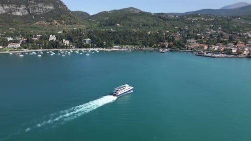 Aerial shot tracking a large boat approaching the coast of Garda, Lake Garda, Italy.