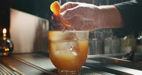 Close up of a professional bartender is squeezing an orange while preparing an alcoholic cocktail