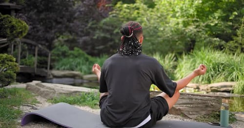 Young African American Spirituality Man Meditating Yoga Asana Sitting in a Park Outdoor Back View