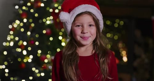 Happy Girl Wearing Santa Hat In Front of Christmas Tree