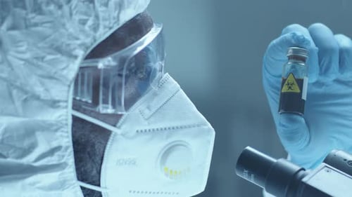 Lab Worker in Protective Overall and Mask Examining Blood in Test Tube