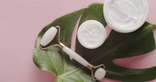 Top view on open jars with cream and massage quartz roller for face