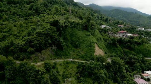 fly over a car moving on an asphalt road through green forest hills