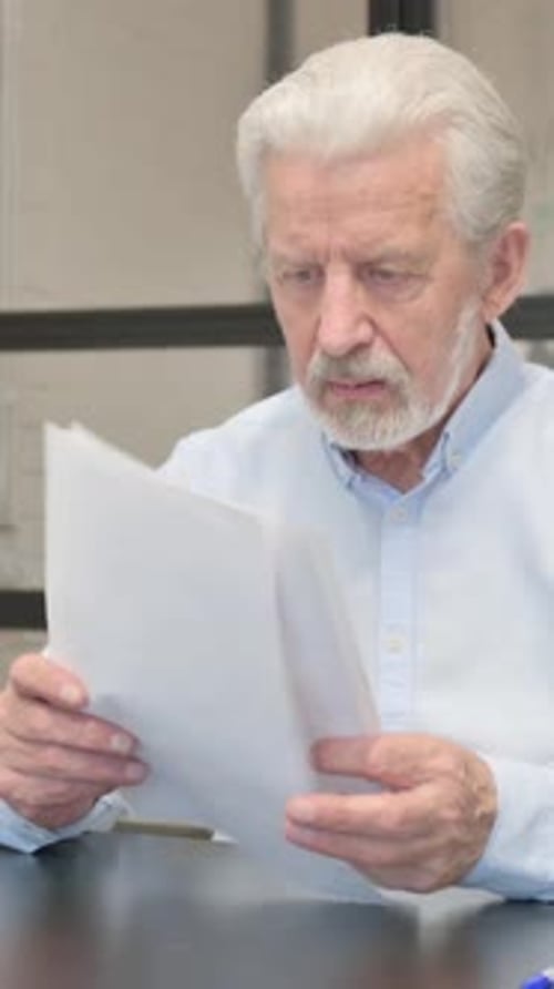 Senior Man Reading Document with Frustration Indoors