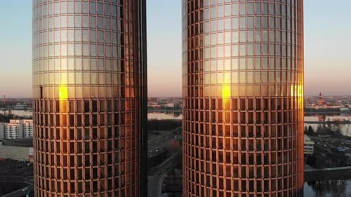 Drohnenblick auf zwei gläserne Wolkenkratzer bei einem goldenen Sonnenuntergang mit Stadtbild im Hintergrund in Riga, L