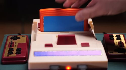 Hand Inserting Cartridge Into Retro Game Console with Controllers