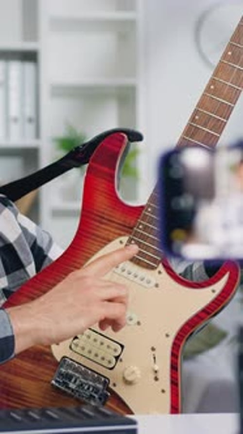 Joven profesor de guitarra hablando con la cámara y mostrando cómo tocar a un bloguero crea una lección tutorial