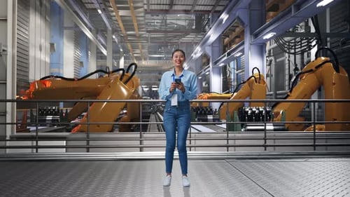 Woman Uses Phone in Factory with Robotic Arms