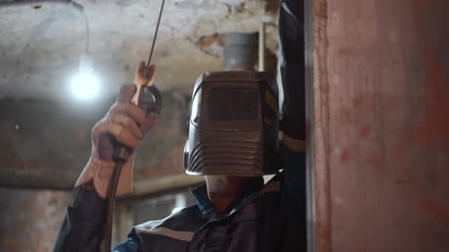 Professional Welder in Safety Suit Puts Protective Mask Down and Welds with Electrode Holder Sparks
