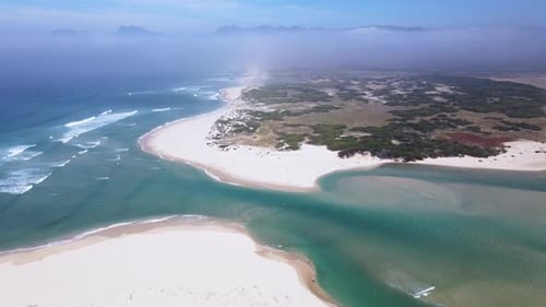 Dramatic drone scene of a river mouth opening up to the ocean with sand dunes and mountains in the d