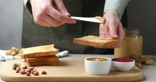 Toast Being Covered with Peanut Butter on Wooden Board