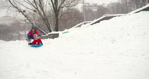 Woman and Child Sledding Down Snowy Hill