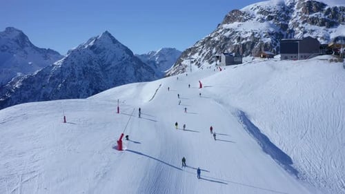 Aerial dolly in over several skiers skiing a snowy slope on top of a mountain on a sunny day