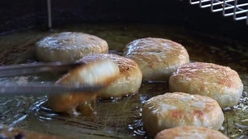Close up shot capturing the food stall vendor uses kitchen tongs to flip the freshly made meat pies,