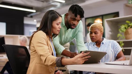Collaborating in office, diverse team discussing project using tablet and laptop