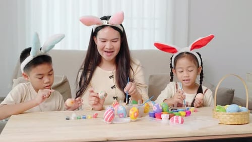 A Mother and Kids with Bunny Ears Happily Paint Easter Eggs at a Table Near a Festive Basket