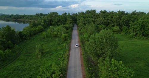 A White Car is Driving Along the Road Going Into the Forest
