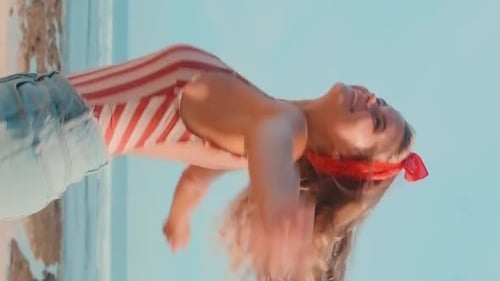 Young Cheerful Cute Caucasian Woman in Denim Shorts Spinning Stands on Beach