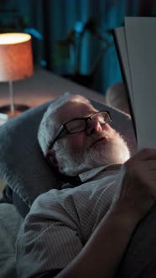 An Elderly Man Lies in Bed and Reads Documents Then Reacting Emotionally