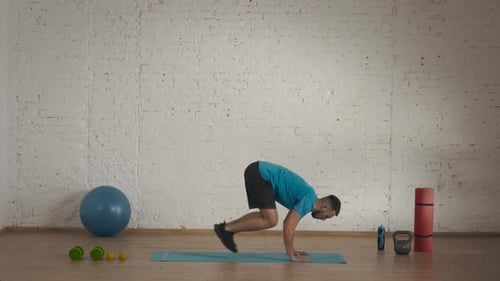 Entraîneur de fitness pour homme en tenue de sport faisant du burpee avec des sauts bas pour un cours en ligne au Home Studio