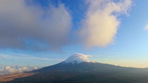 Aerial drone view of Mount Fuji with snow at the top and clouds moving around in daylight