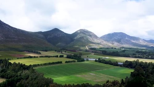 Aerial drone shot panning to reveal the lush green fields and fertile farmlands in the valley surrou