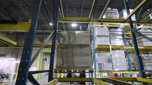 Un chariot élévateur soulève une palette sur un support d'entrepôt