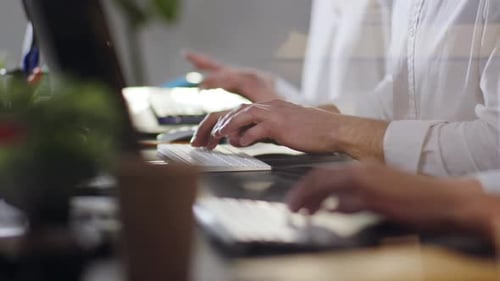 Seitliche Nahaufnahme von Mitarbeitern, die in einem hellen, modernen Büro mit Tastaturen auf ihren Computern tippen