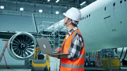 Asian Male Engineer Looking At A Laptop And Looking Around While Aircraft Maintenance