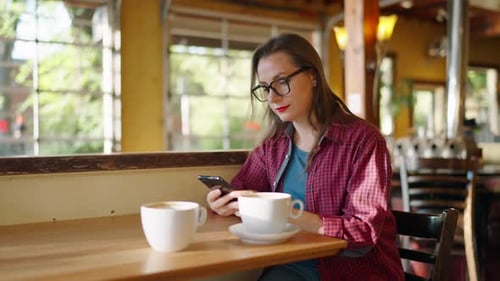 Woman is Using Smartphone and Drinking Coffee in the Cafe