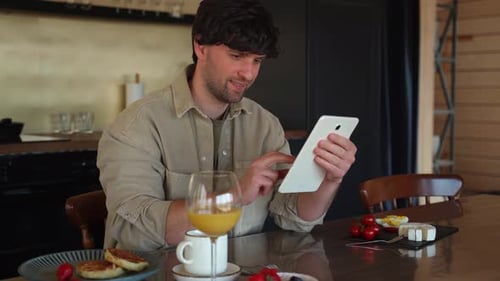 Man Works on a Tablet Uses Free Internet Access Drinks Orange Juice and Eats a Delicious Breakfast