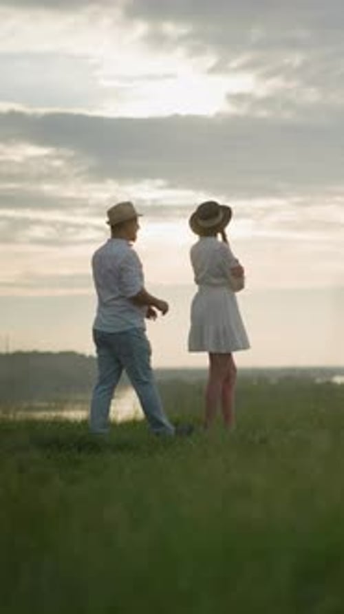 Man Approaches and Embraces Woman on Grassy Hill at Sunset