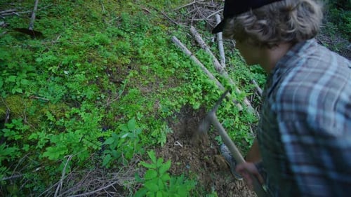 Ein Mann gräbt mit einer Spitzhacke ein Loch in einem Wald