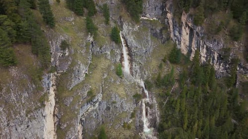 Stunning aerial view of a waterfall cascading down rocky cliffs in the Dolomite mountains, surrounde