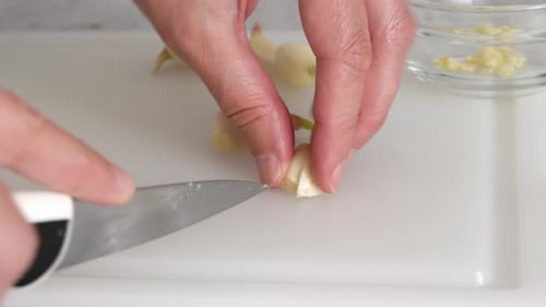 The chef chopping garlic on a white plastic cutting board