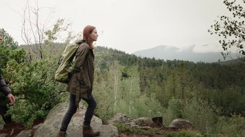A beautiful female hiker and boy hiker climb a rock and look at mountains.