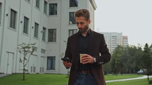 Man Checks Phone While Enjoying Coffee Outside Modern Building in the City