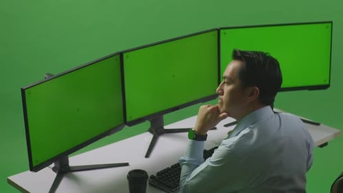 Side View Of Asian Man Thinking With Mock Up Multiple Computer Monitor In Green Screen