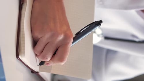 Doctor Writes in Notebook Journal at the Workplace