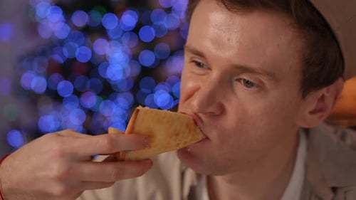 Headshot of Sad Bored Man Eating Pizza Slice Sighing Looking Away at Background of Christmas Light