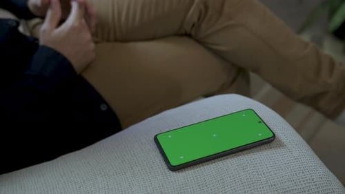 Man Sitting On Couch, Holds Phone With Green Screen App During Discussion. closeup shot
