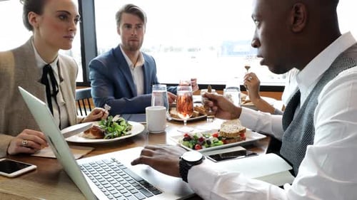 Business lunch at restaurant with laptop and multiethnic group working together