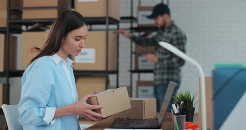 Woman Packs Boxes and Uses Laptop in Office