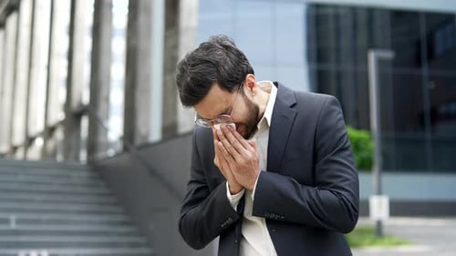 Young Man Blowing Nose with Tissue Outdoors