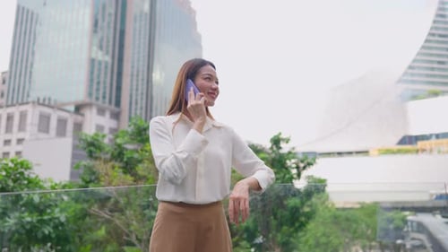 Asian young businesswoman talking on smartphone while standing in city.