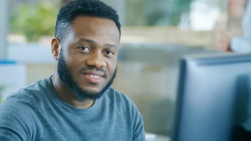 Young Black Man Works on a Personal Computer Charmingly Smiles on Camera. Stylish Smart Man with a