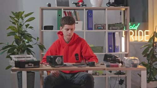 Footage of Young Caucasian Man in Red Casual Clothes Sitting at Desktop and Starts Working on