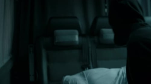 Un criminel masqué ligote un otage inconscient dans un camion