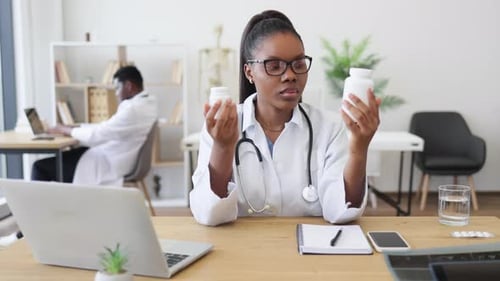 Woman Doctor Comparing Two Medicine Bottles at Desk