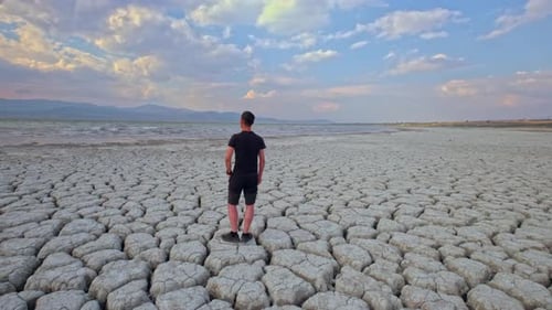 Young Adult Standing on cracked earth near water